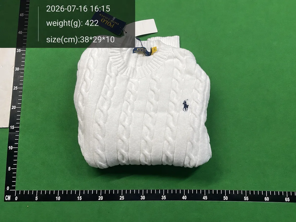 Folded white cable-knit jumper photographed on a warehouse inspection surface