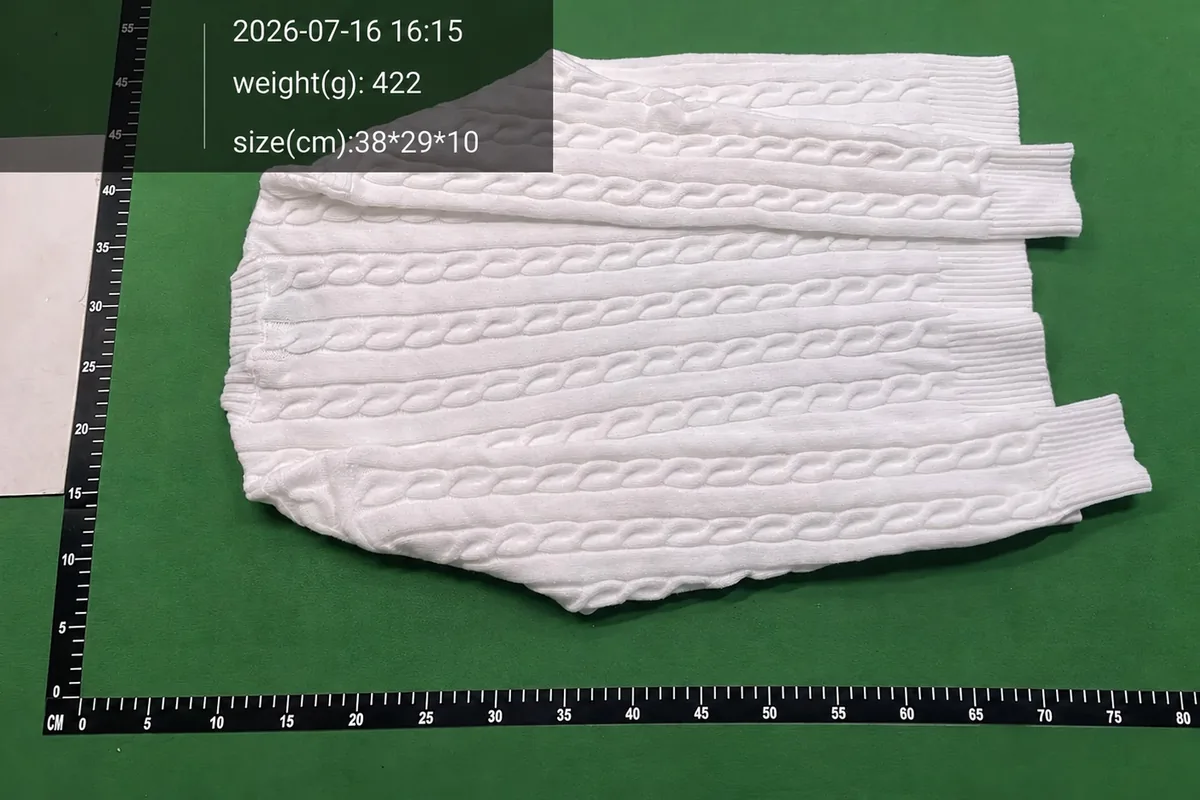 Reverse view of the white cable-knit jumper on a measured warehouse surface